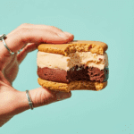 A hand holding a finished Peanut Butter Chocolate Sorbet Sandwich with a bite taken out.