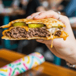 A hand holding a Cheeseburger Quesadilla with a bite taken out.