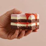 A hand holding a square of a Frozen Brownie Sundae with a bite taken out.