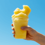 A hand squeezing a finished Limber de Coco y Piña from a plastic cup.