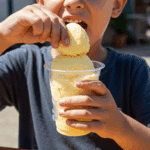 A child eating a finished Limber de Crema by squeezing it from a plastic cup.