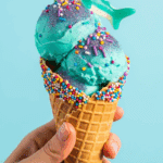 A cone of homemade Mermaid Ice Cream topped with a gummy shark.