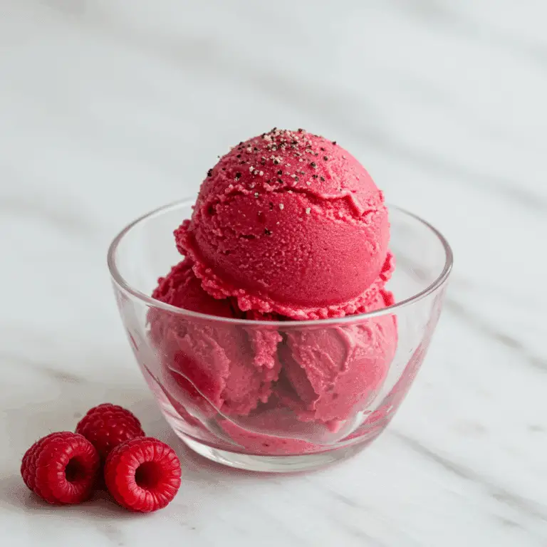 A scoop of homemade Raspberry Buttermilk Sherbet garnished with black pepper.