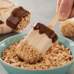 Dipping a finished Cereal Ice Pop in a crushed cereal topping.