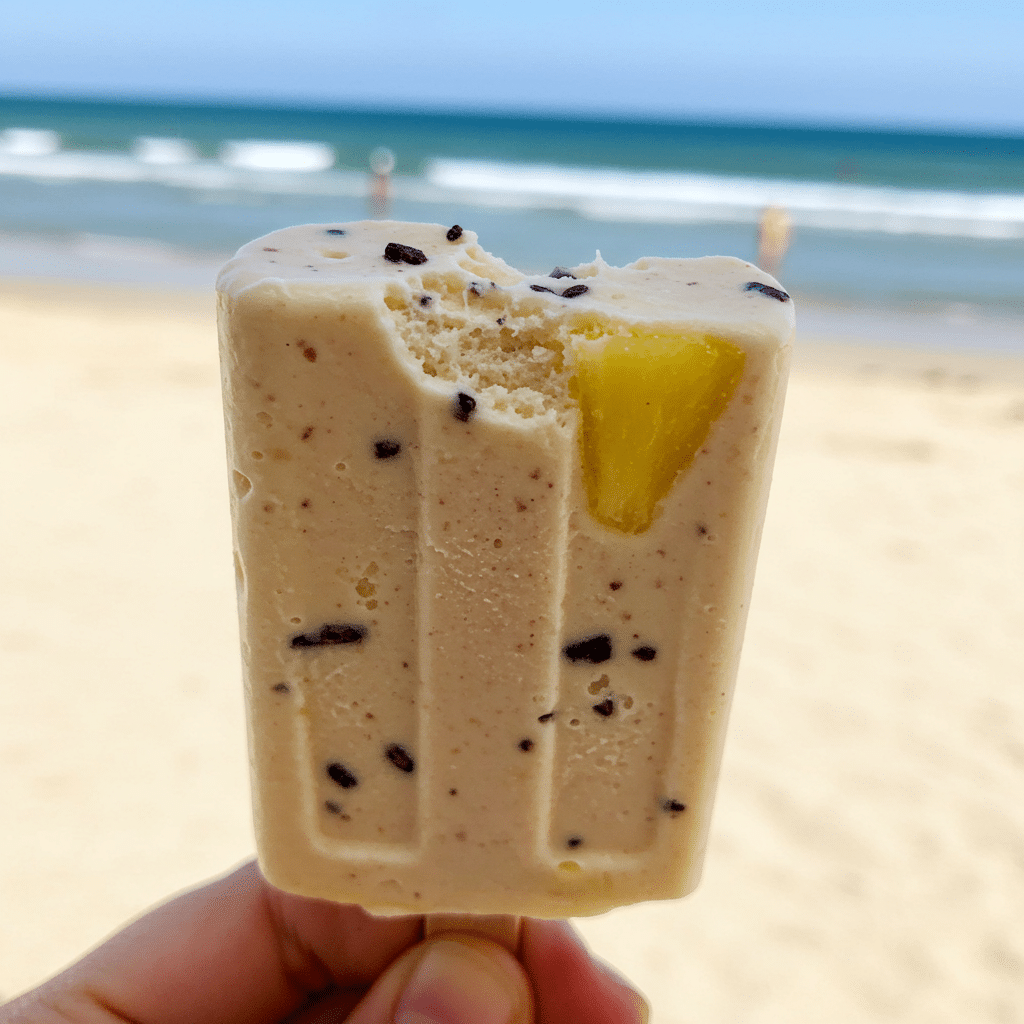 A hand holding a Cocoa Colada Ice Pop with a bite taken out to show the texture.