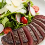 A plated meal of the sliced cocoa-rubbed steak and a fresh side salad.