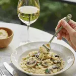 A person enjoying a sophisticated lunch of Creamy Orzo with Mushrooms and white wine.