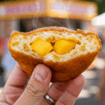 A hand holding a warm, fluffy homemade Peach Fritter broken in half to show the inside.