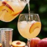 Pouring a glass of refreshing White Peach Sangria from a pitcher at a summer party.