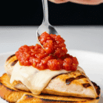 Spooning the fresh tomato sauce over the finished Grilled Chicken Parmesan.