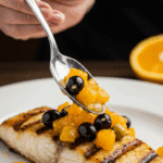 Spooning the fresh orange and olive salsa over the finished Grilled Striped Bass.