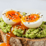 A slice of avocado toast topped with two halves of a perfect Jammy Egg.
