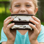 A child's hands holding a large, homemade Oreo Ice Cream Sandwich on a summer day.