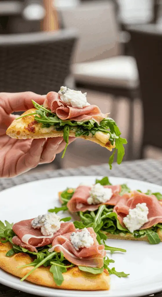 A hand holding a slice of the finished Prosciutto Arugula Flatbread.