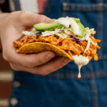 A hand holding a finished Pulled Chicken Tostada.