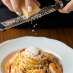 Grating fresh Parmesan cheese over a bowl of the finished Shrimp Pasta with Cream Sauce.