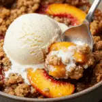 A close-up of a warm bowl of Juicy Peach Crisp with a scoop of vanilla ice cream melting on top.