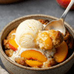 A cozy bowl of warm Peach Bread Pudding with a scoop of melting vanilla ice cream and caramel sauce.