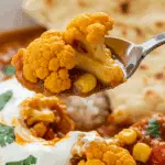 A spoonful of the finished Tomato-Cauliflower Curry with a piece of naan