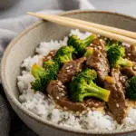A cozy bowl of homemade Beef and Broccoli served over a bed of fluffy white rice with chopsticks.