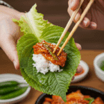 A person's hands using chopsticks to make a traditional Korean lettuce wrap (ssam) with a piece of homemade bulgogi.