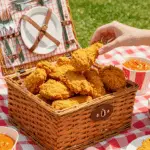 A basket of crispy Buttermilk Fried Chicken being enjoyed at a happy summer picnic.