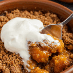 A close-up of a warm bowl of Pumpkin Crumble with a large dollop of whipped cream melting on top.