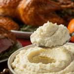 A large, beautiful bowl of Creamy Garlic Mashed Potatoes being served as a side dish at a festive holiday dinner.
