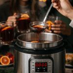 A hand ladling a hot mug of mulled wine from the Instant Pot at a festive holiday party.