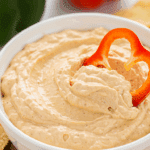 A hand dipping a fresh red bell pepper slice into a healthy, high-protein Cottage Cheese Taco Dip.