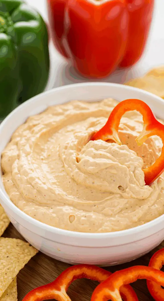 A hand dipping a fresh red bell pepper slice into a healthy, high-protein Cottage Cheese Taco Dip.