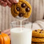 A hand dunking a warm, homemade Pumpkin Chocolate Chip Cookie into a tall, cold glass of milk.