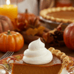 A perfect slice of homemade Pumpkin Pie with a large swirl of whipped cream being served for a holiday dessert.