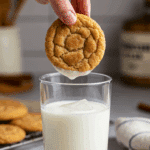 A hand dunking a warm, homemade Snickerdoodle cookie into a tall, cold glass of milk.