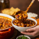 A large pot of homemade Vegetarian Pumpkin Chili being served at a fun fall party with a toppings bar.