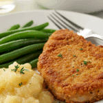 A fun, kid-friendly dinner plate with a homemade, crispy Baked Breaded Pork Chop, served with applesauce and green beans.