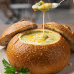 A cozy, hollowed-out sourdough bread bowl filled with homemade, creamy Broccoli Cheddar Soup.