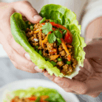 A hand holding a beautiful, overflowing, homemade Asian Lettuce Wrap, about to take a bite.