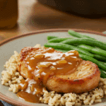 A classic dinner plate with a thick, saucy pork chop served over a bed of brown rice with a side of green beans.