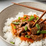 A cozy bowl of homemade Spicy Beef Stir Fry served over a bed of fluffy white rice with chopsticks.