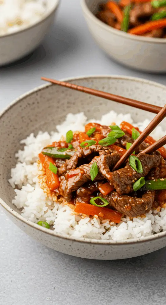 A cozy bowl of homemade Spicy Beef Stir Fry served over a bed of fluffy white rice with chopsticks.