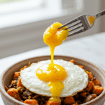 A cozy bowl of homemade, healthy Sweet Potato Hash with a perfect, runny-yolked egg being broken open with a fork.