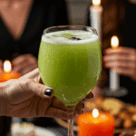 A hand holding an elegant glass of a homemade, green, and spooky "Bubbling Cauldron" Punch at a fun and sophisticated Halloween party.