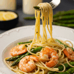 An elegant plate of homemade, saucy Sheet Pan Shrimp and Asparagus served over a bed of thin spaghetti for a sophisticated dinner.