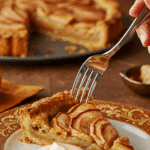 A beautiful plate of a homemade, elegant, and flaky slice of a French Apple Tart, being served with a large dollop of crème fraîche at a Thanksgiving dinner.