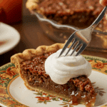 A beautiful plate of a homemade, elegant, and flaky slice of a Pecan Pie, being served with a large dollop of whipped cream at a Thanksgiving dinner.