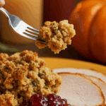 A beautiful plate of a homemade, elegant, and crispy-topped Sausage and Apple Stuffing, being served with a thick slice of a roasted turkey at a Thanksgiving dinner.
