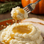 A beautiful plate of a homemade, elegant, and silky-smooth Mashed Potatoes, being served with a thick slice of a roasted turkey and gravy at a Thanksgiving dinner.