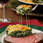 A beautiful plate of a homemade, elegant, and crispy-topped Spinach Gratin, being served with a thick slice of a prime rib at a holiday dinner.