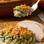 A beautiful plate of a homemade, elegant, and crispy-topped Green Bean Casserole, being served with a thick slice of a roasted turkey at a Thanksgiving dinner.
